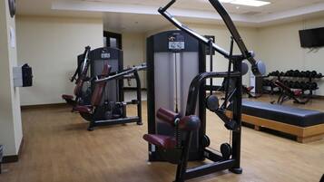 Un gimnasio con equipo de ejercicio, una banca y un televisor instalado en la pared.