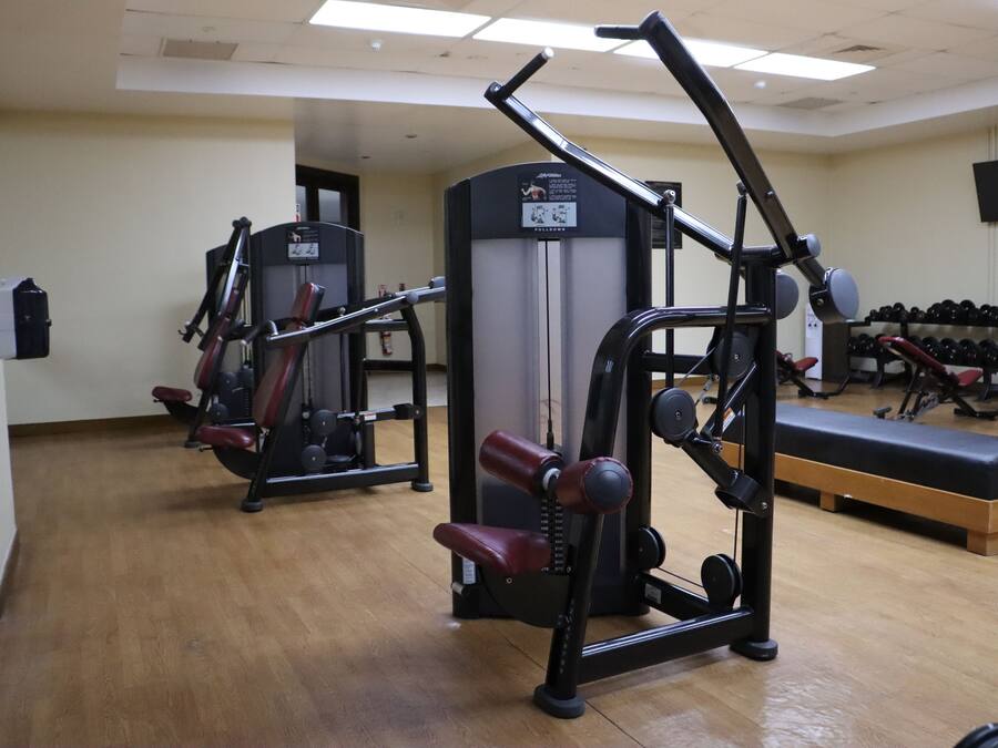 Un gimnasio con equipo de ejercicio, una banca y un televisor instalado en la pared.