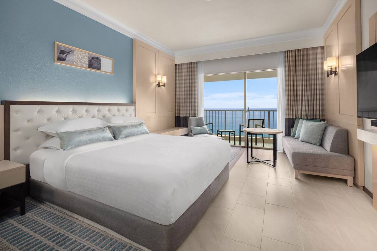 A hotel room with a large bed, a sofa, a small table, and a TV.