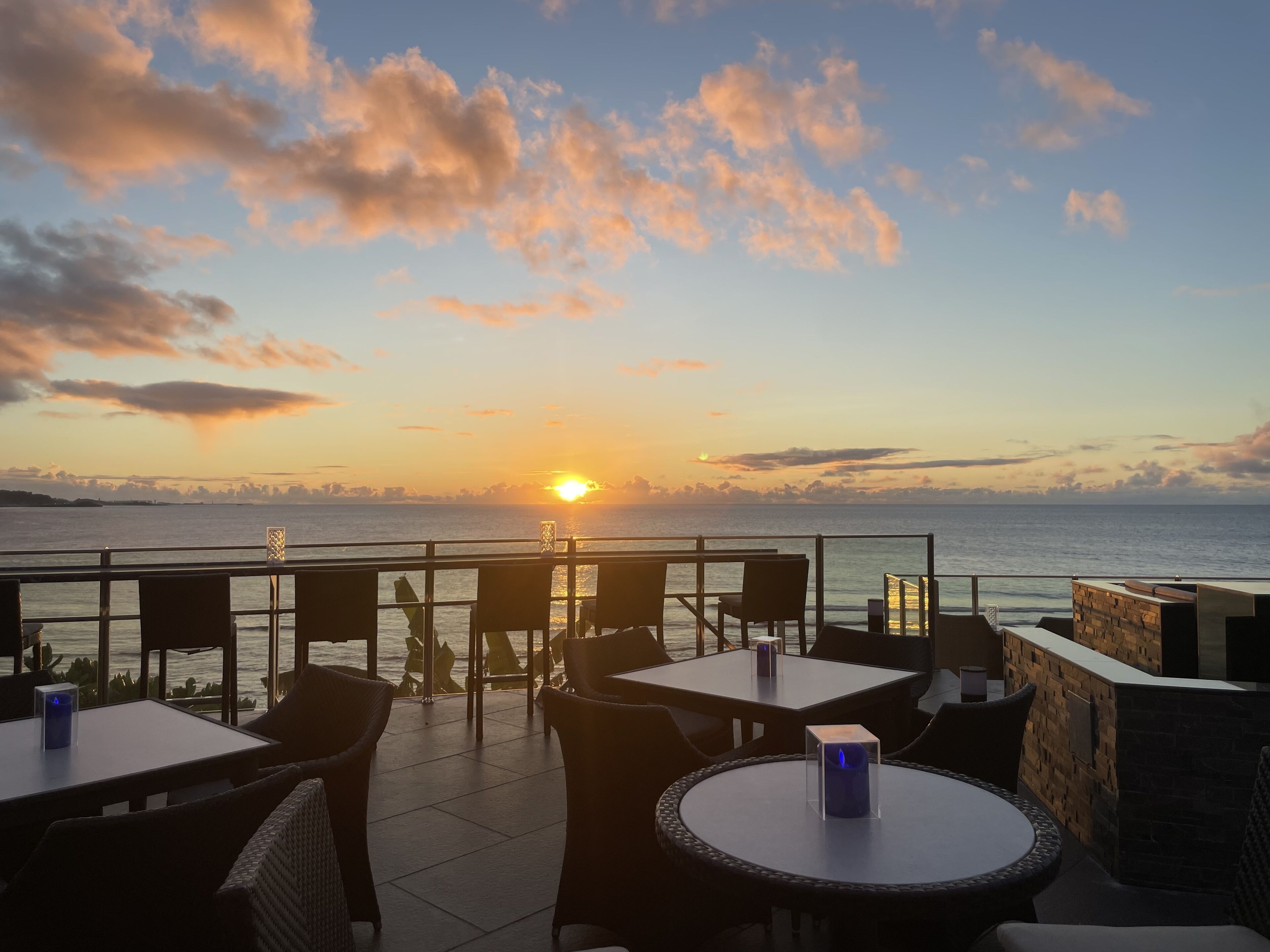 Una terraza con mesas y sillas que da al mar al atardecer.