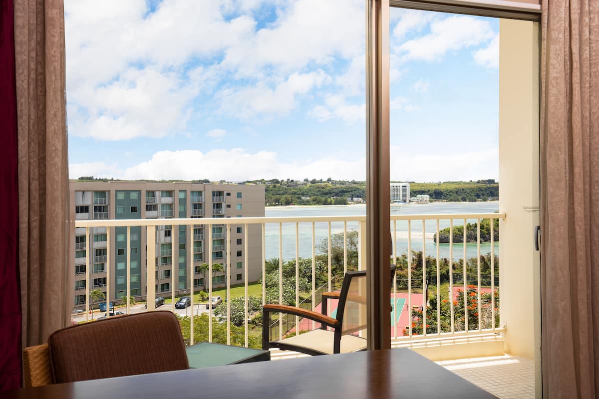 A balcony with a view of a body of water, a building in the background, and a table with chairs.