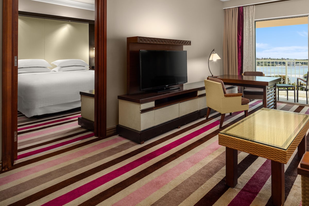 A hotel room with a bed, a television, a seating area with a table and chairs, and a view of the outdoors.