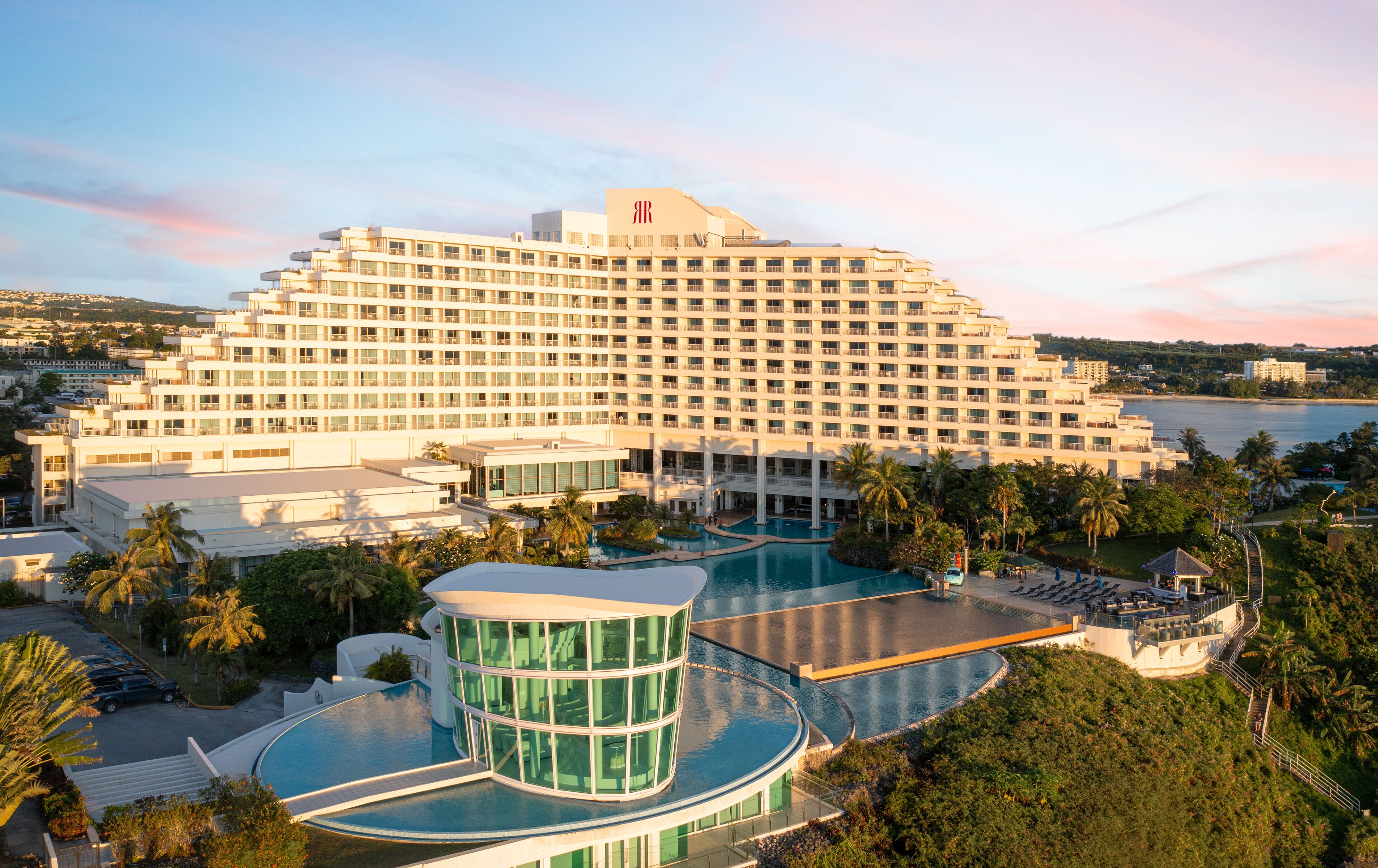 A large hotel with multiple floors, a central courtyard with a pool, and a view of the sea.