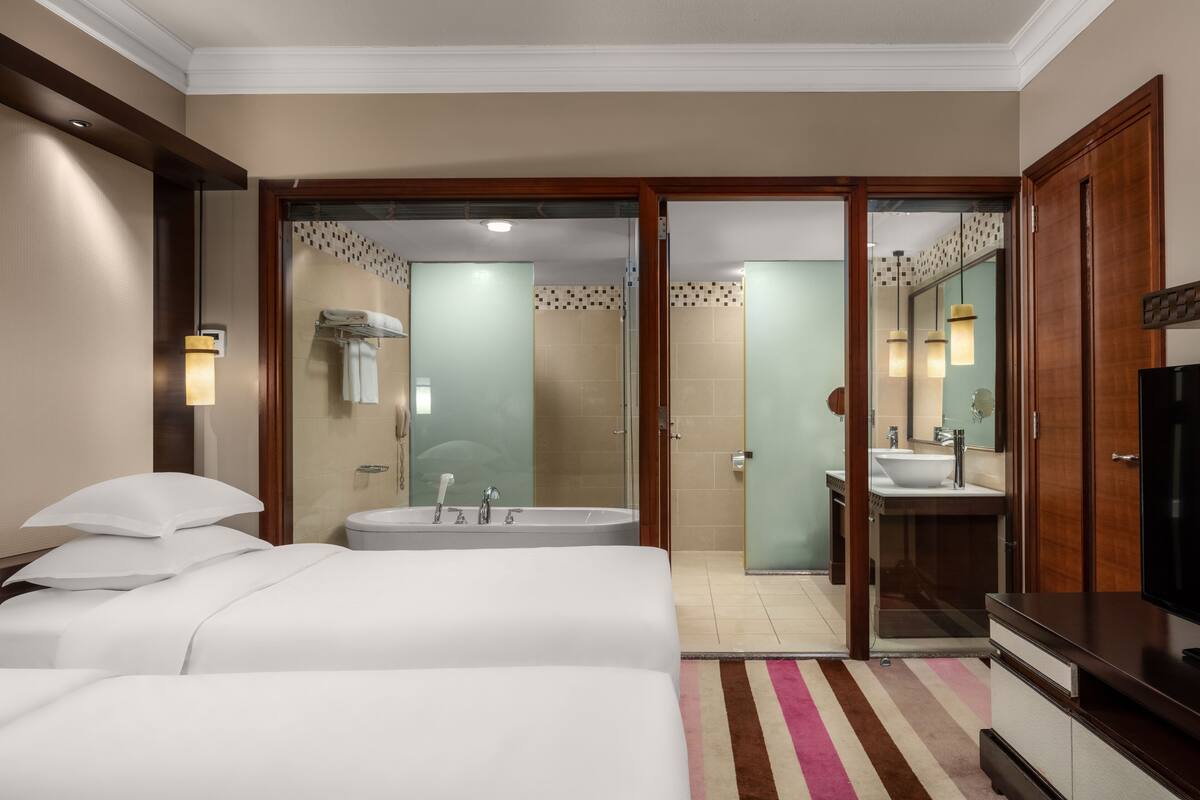 A hotel room with a large bed, a separate bathroom with a bathtub, a vanity with a mirror, and a television.