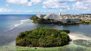A coastal resort with multiple high-rise buildings, a small island with lush greenery, and clear blue waters.