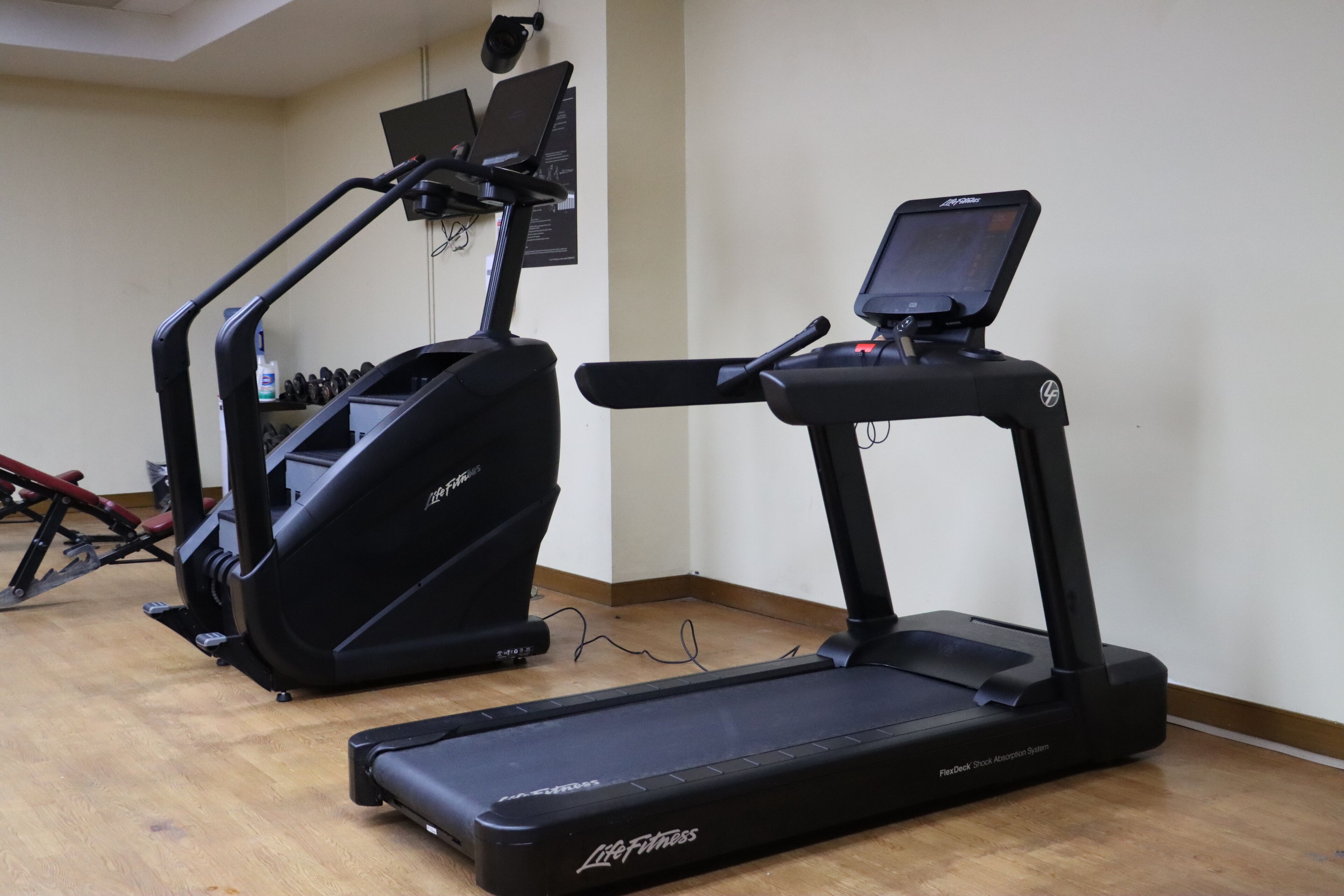 A gym with two treadmills, a weight bench, and a wall-mounted TV.
