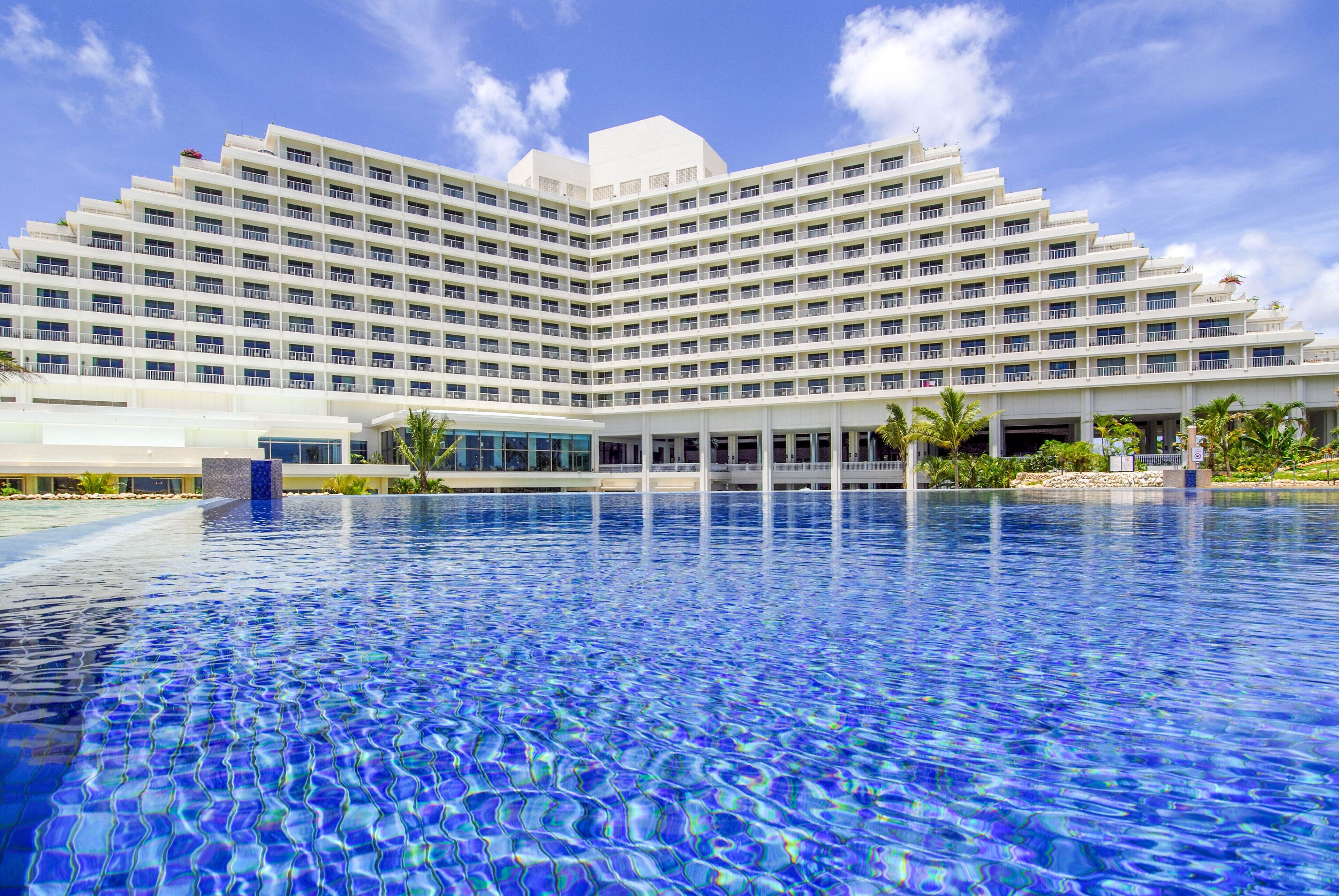 Un hotel grande con un diseño moderno, que cuenta con un amplio área de piscina al frente.