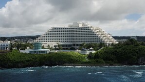 A large, multi-story hotel with a modern design, located near a coastline with lush greenery and a view of the ocean.