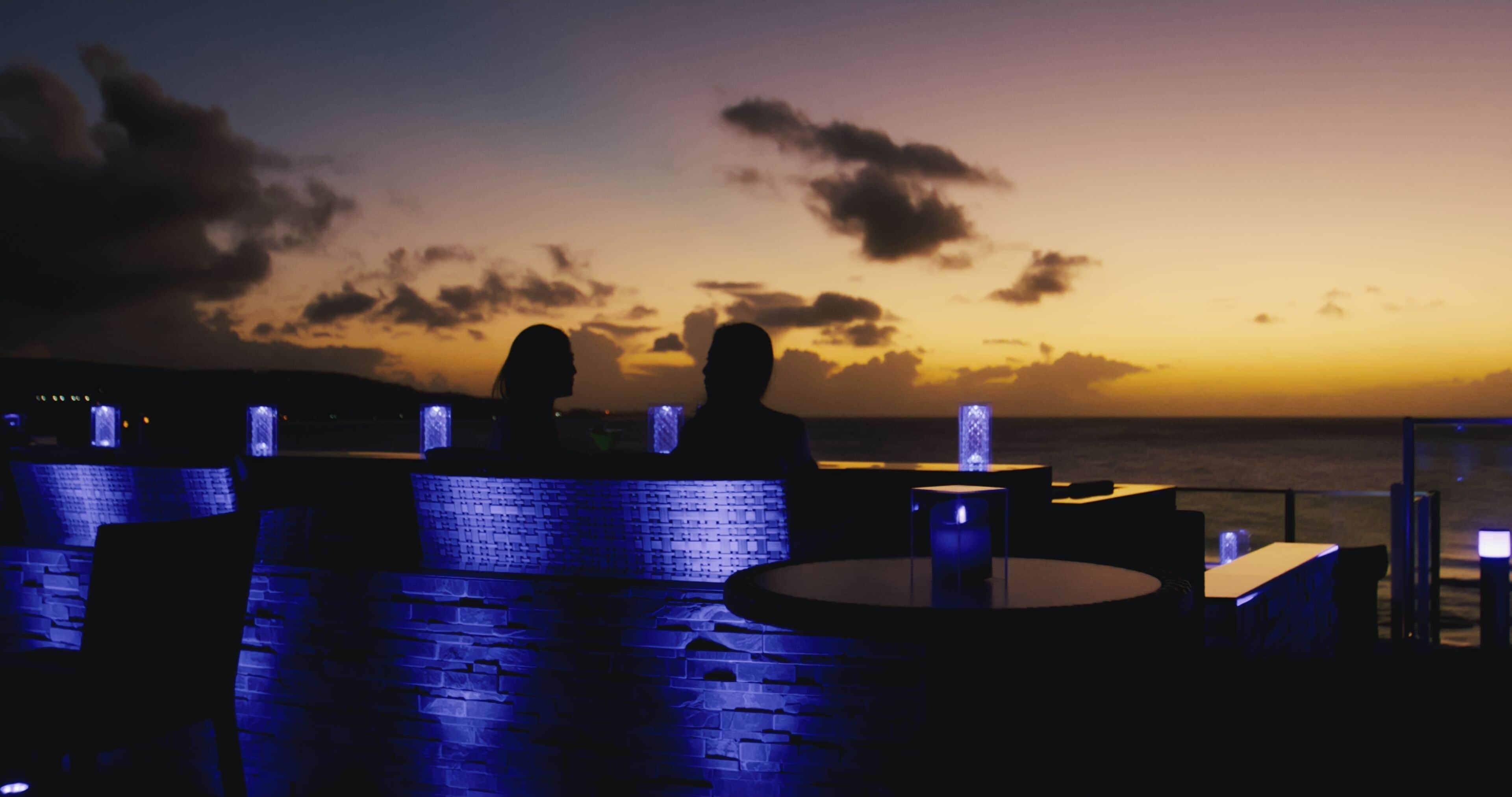 A sunset view from a rooftop terrace with stone walls and blue lighting.