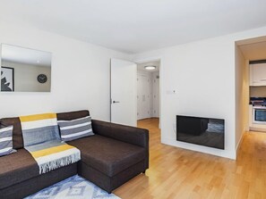 Een moderne woonkamer met een donkerbruine bank, een flatscreen televisie aan de muur en een houten vloer.