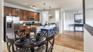 A modern kitchen with wooden cabinets, a stainless steel refrigerator, and a dining area with a round table and chairs. - ★SPACIOUS 4BD/2BA★CONVENTION CENTER/ UNIVERSAL EPIC UNIVERSE WALKING DISTANCE (Orlando)