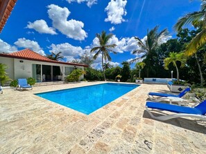A swimming pool with blue water, surrounded by lounge chairs and palm trees.