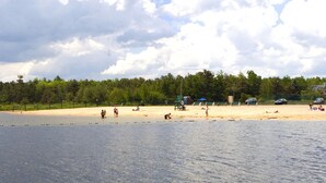 Une plage avec un rivage sablonneux, une étendue d’eau au premier plan et une zone boisée en arrière-plan.