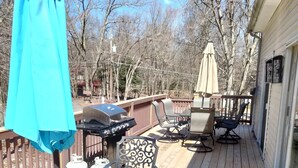 Une terrasse en bois aménagée avec du mobilier d’extérieur, notamment une table et des chaises, ainsi qu’un barbecue.