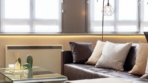 A modern living room with a leather sofa, a glass coffee table, and a minimalist decor including a cactus and a geometric lamp. - Lawrence House by Interhome (London City)
