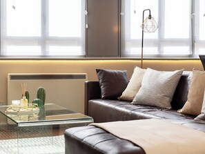 A modern living room with a leather sofa, a glass coffee table, and a minimalist decor including a cactus and a geometric lamp.