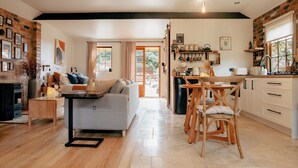 Una sala de estar acogedora con sofá, mesa de centro y comedor con sillas. Hay una cocina con lavaplatos y armarios.