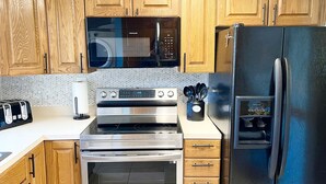 Una cucina con mobili in legno, un frigorifero in acciaio inossidabile, un forno a microonde, un forno e un tostapane.