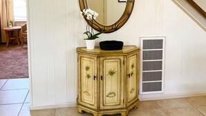 Una stanza con un grande specchio ovale, un armadietto in legno con decorazioni intagliate, una pianta in vaso e un quadro appeso al muro.
