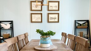 Zona pranzo con un tavolo di legno lungo, runner blu e sedie. Si nota un centrotavola con piante decorative e quadri appesi al muro.
