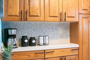 Kitchen area with a coffee maker, sugar container, and two mugs on the countertop.