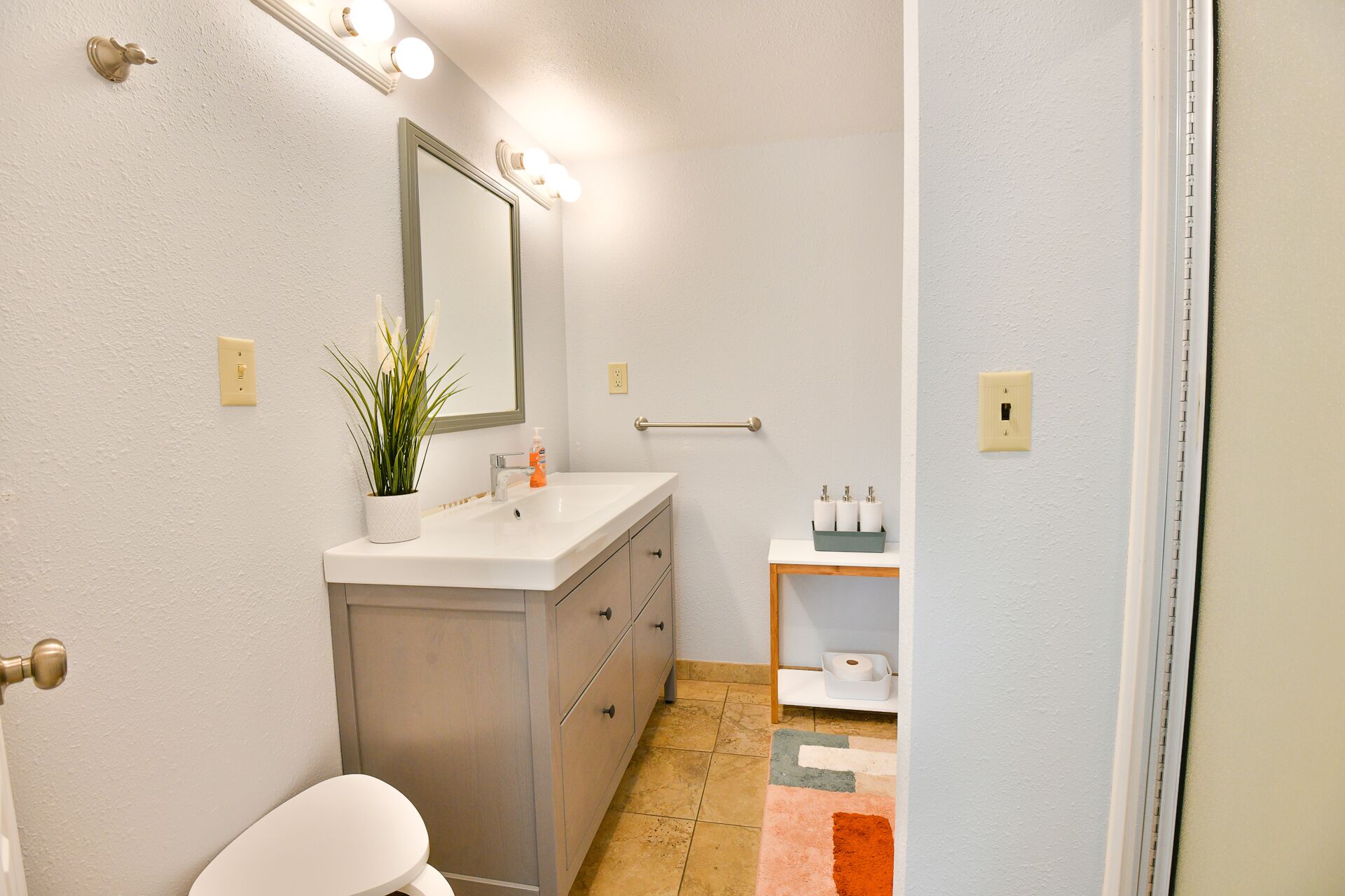 Une salle de bain avec un lavabo blanc, un miroir, des toilettes et une petite étagère contenant des articles de toilette.
