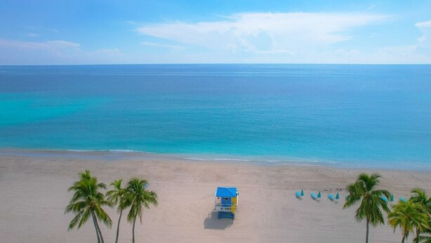 A beach with a lifeguard tower, palm trees, and a clear view of the ocean. - CH Luxury Spacious Beach Condo | Ocean Breeze-CS40 (Hollywood)