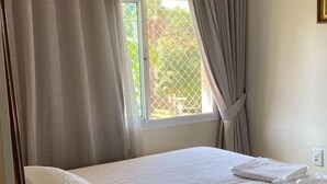 A neatly made bed with white linens and pillows, a ceiling fan, and a window with curtains. - The Sun (2 bedrooms in the heart of Brasilia) (DF)