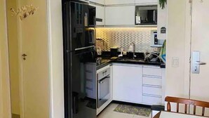 A compact kitchen with white cabinets, a black refrigerator, a microwave, and a sink. - The Sun (2 bedrooms in the heart of Brasilia) (DF)