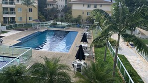 A swimming pool with a wooden deck, surrounded by palm trees and a white fence. - The Sun (2 bedrooms in the heart of Brasilia) (DF)
