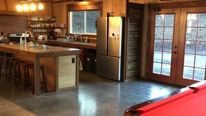 A spacious kitchen with a central island, stainless steel appliances, and a view through large windows. - Fun Family Private Retreat with lighted Sports Court and Pool (Ocean View)