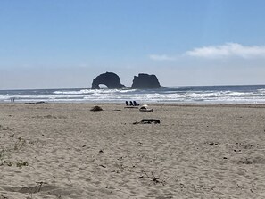 A sandy beach with two rock formations in the distance and a few people and sun loungers in the foreground.