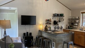 A modern kitchen with a bar area, a flat-screen TV, and a dining area with a sofa and bar stools.