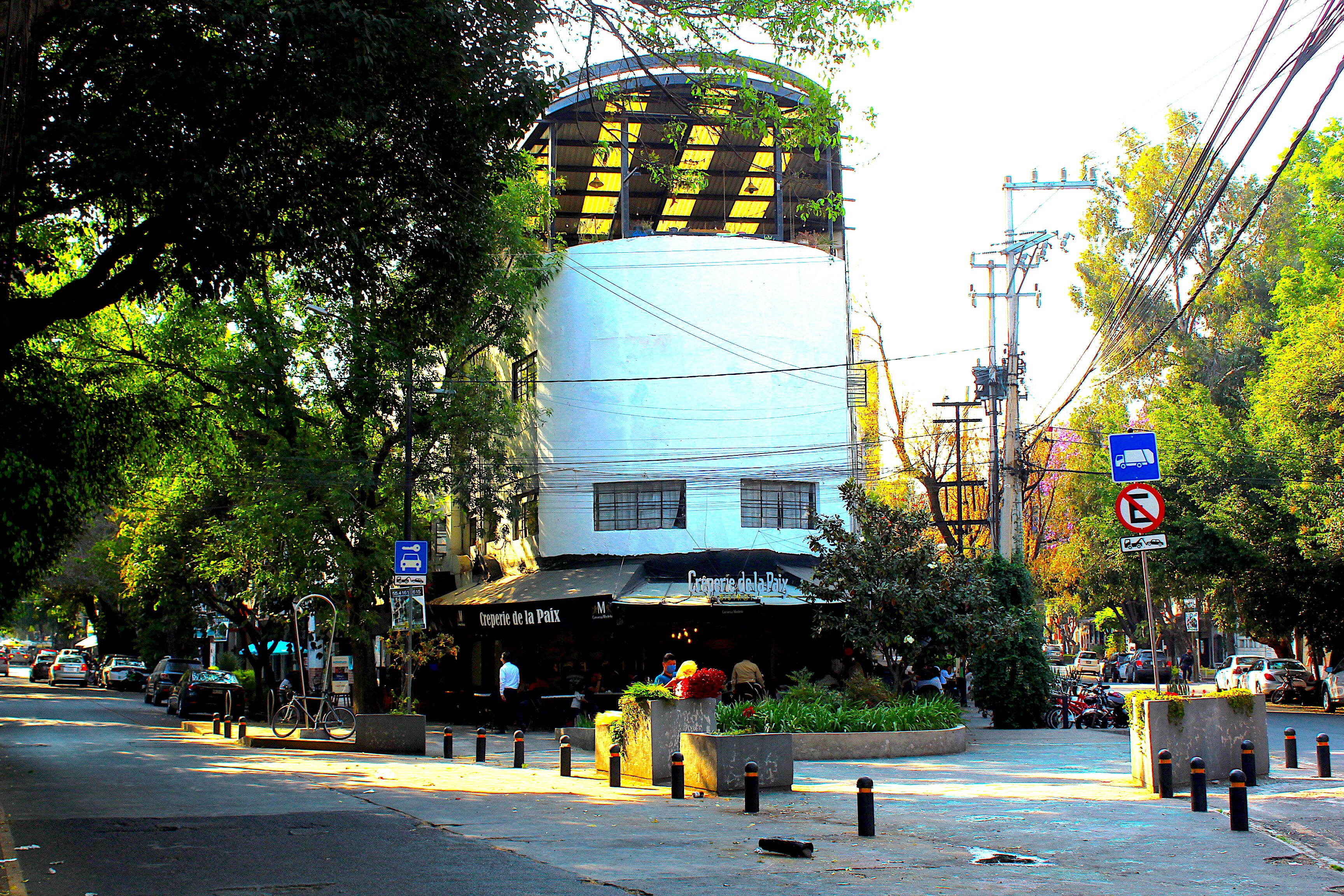 A building with a curved facade, a restaurant with outdoor seating, and a street with cars and pedestrians.