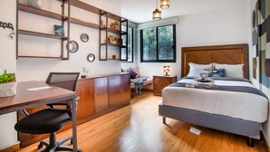 A modern bedroom with a wooden desk, a bed with a headboard, a nightstand, and a window with a view of trees. - Comfortable Room in Condesa + Rooftop & Coworking - Gamma by Nomadier (Ciudad de México)