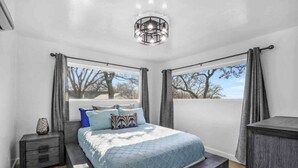 A bedroom with a bed, bedside tables, a nightstand, a dresser, and a window with curtains. - Rare Modern Beachfront Lake House on Lewisville Lake with Hot Tub, Deck & BEACH (Little Elm)