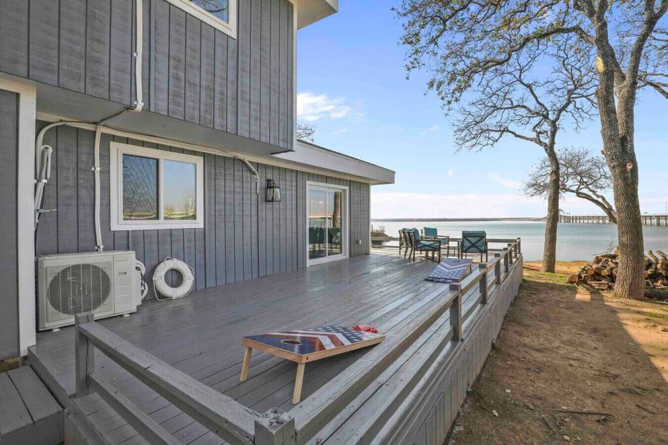 A modern two-story house with a wooden deck, outdoor seating, and a view of the water.