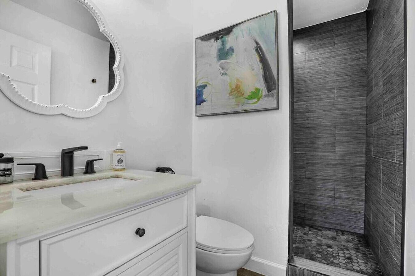 Un bagno con un mobile lavabo bianco, un water e una doccia rivestita di piastrelle scure.