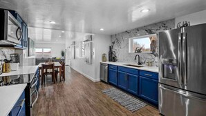 A modern kitchen with blue cabinets, a stainless steel refrigerator, and a marble backsplash. - Rare Modern Beachfront Lake House on Lewisville Lake with Hot Tub, Deck & BEACH (Little Elm)