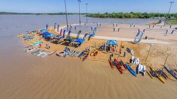 Luchtbeeld van een strand met vele kajaks en kano's op de zandstrook, waarbij enkele mensen in de buurt staan.