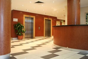 Check-in and unwind in our welcoming lobby, featuring a reception desk, elevators, and a beautiful potted plant.
