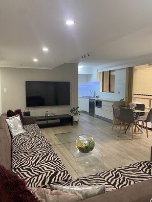 Relax in this stylish living space with a large flat-screen TV, comfortable sofa, and glass coffee table.