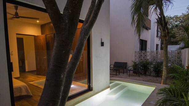 A modern hotel room with a glass door leading to a balcony, a small pool, and a seating area with outdoor furniture. - Tannah Luxury Villa Encanto (Mérida)