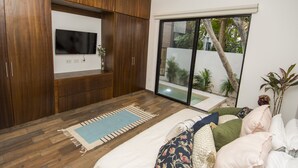 A modern bedroom with wooden cabinetry, a flat-screen TV, a large sliding glass door leading to a balcony, and a cozy bed with patterned bedding. - Tannah Luxury Villa Encanto (Mérida)
