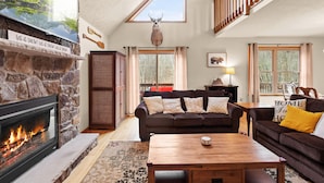 A cozy living room with a stone fireplace, a large flat-screen TV, a wooden ceiling, and a mounted deer head. - “THE ONE” Chalet, Perfect Getaway w/ Hot Tub, Multicade, Pool Table (Albrightsville)