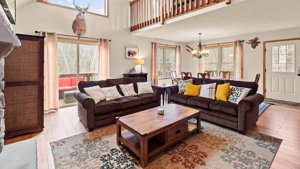 A spacious living room with a high ceiling, wooden staircase, and large windows. - “THE ONE” Chalet, Perfect Getaway w/ Hot Tub, Multicade, Pool Table (Albrightsville)