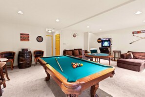 A pool table in a room with a dartboard, a television, and a couch.
