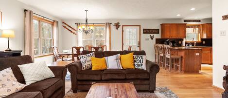 A living room with a brown sofa, a coffee table, and a dining area with chairs and a table.