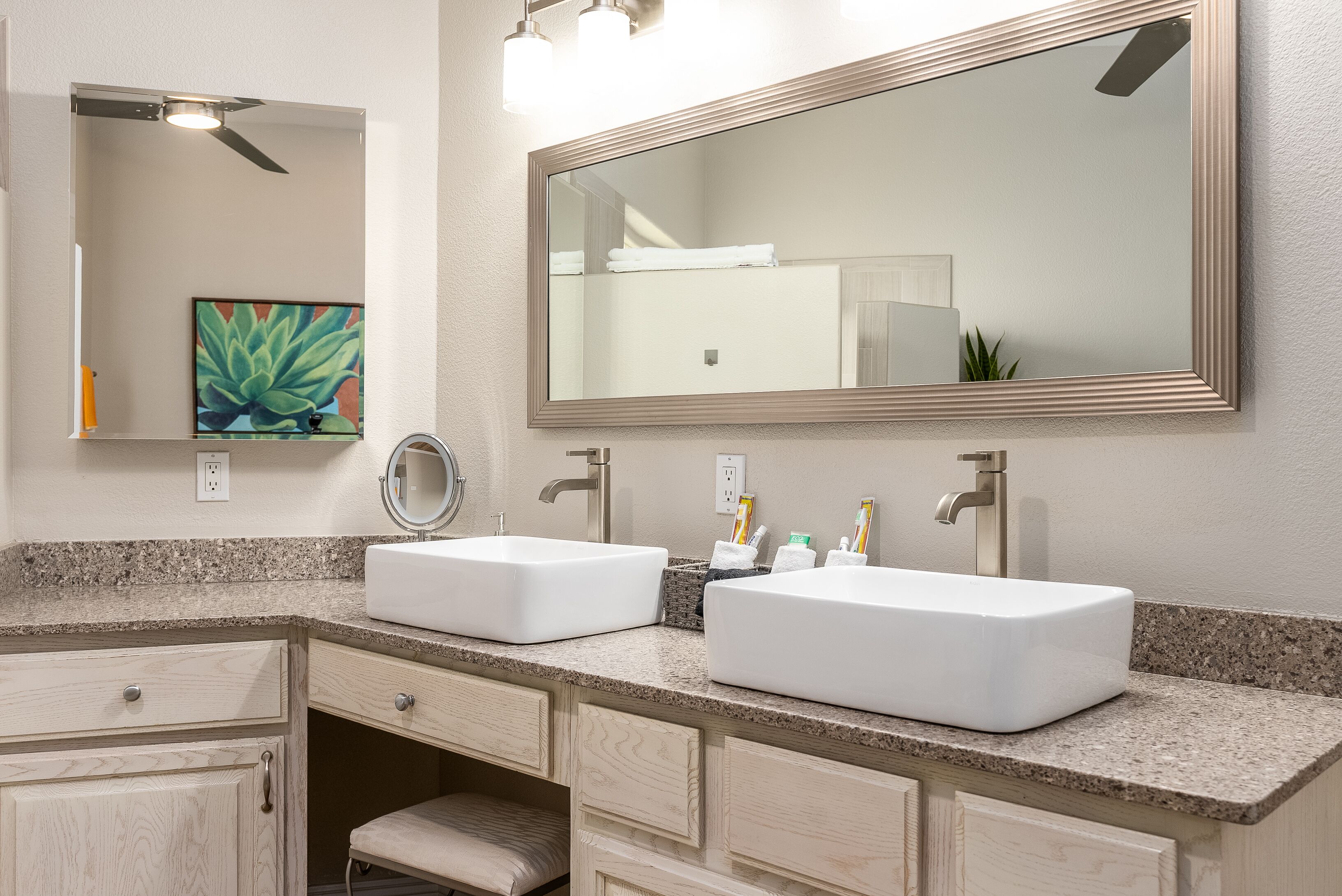 A bathroom with two sinks, a large mirror, a ceiling fan, and a painting on the wall.