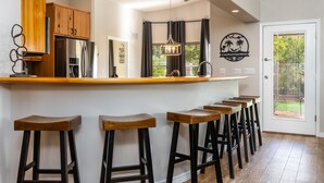 Une cuisine dotée de meubles en bois, d’un réfrigérateur en acier inoxydable, d’un coin bar avec des tabourets et d’une vue sur l’extérieur grâce à une fenêtre.